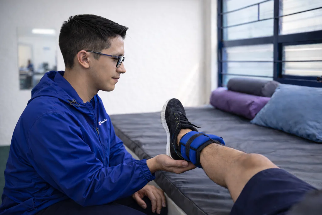 Fisioterapeuta supervisando ejercicio de rehabilitación de rodilla en paciente con pesas de tobillo en clínica de fisioterapia en Toluca